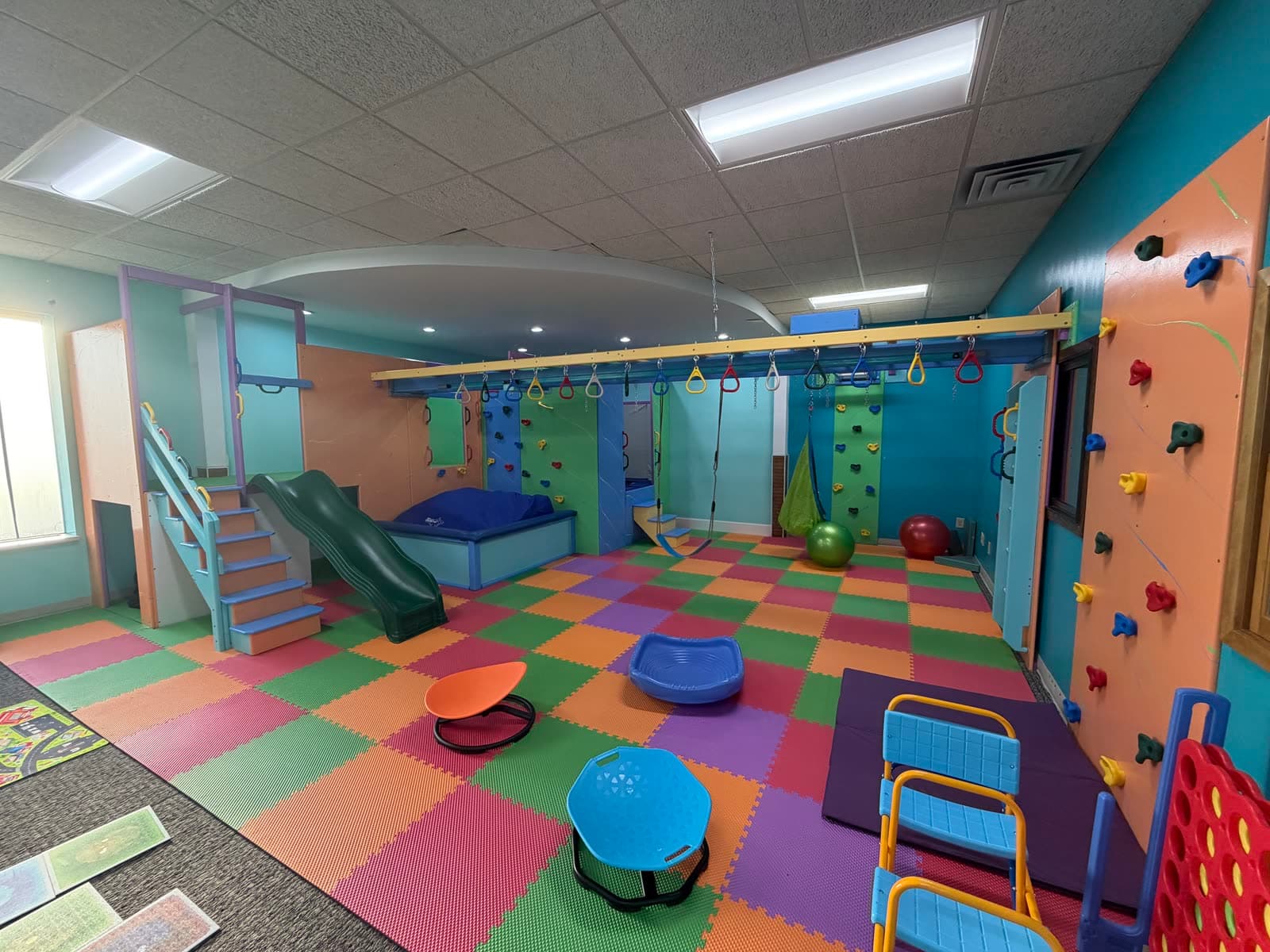The full sensory gym — climbing wall, hanging rings, swings, crash pad, and colorful padded flooring