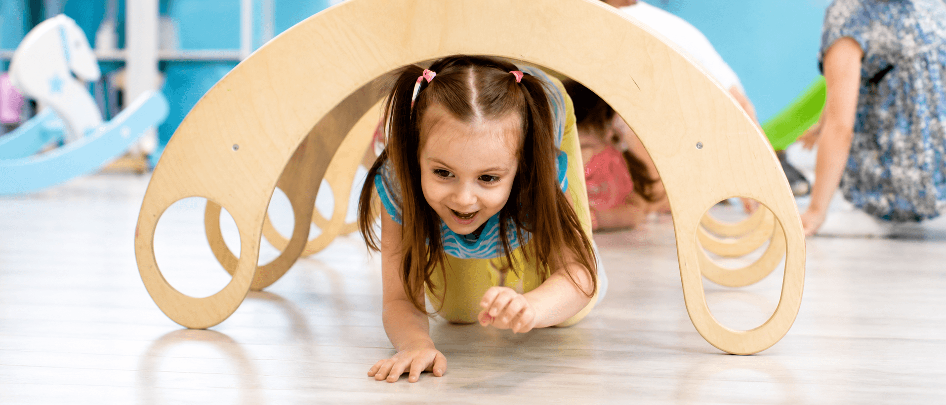 Smiling girl crawling through a wooden play arch in the Active Care Center sensory gym
